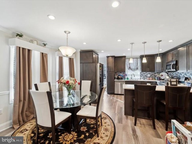 dining space featuring light wood-type flooring, sink, and ornamental molding