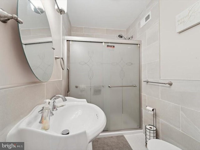 bathroom with tile walls, a shower with shower door, and sink