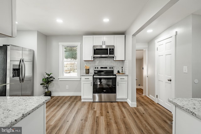 kitchen featuring decorative backsplash, white cabinetry, light stone counters, and appliances with stainless steel finishes