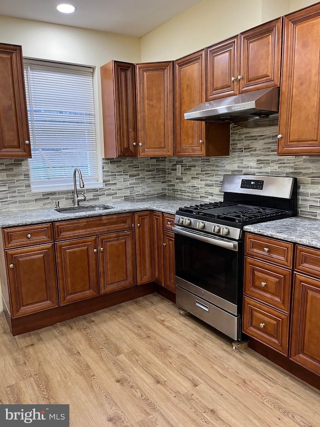 kitchen with gas stove, light stone counters, sink, and light hardwood / wood-style flooring