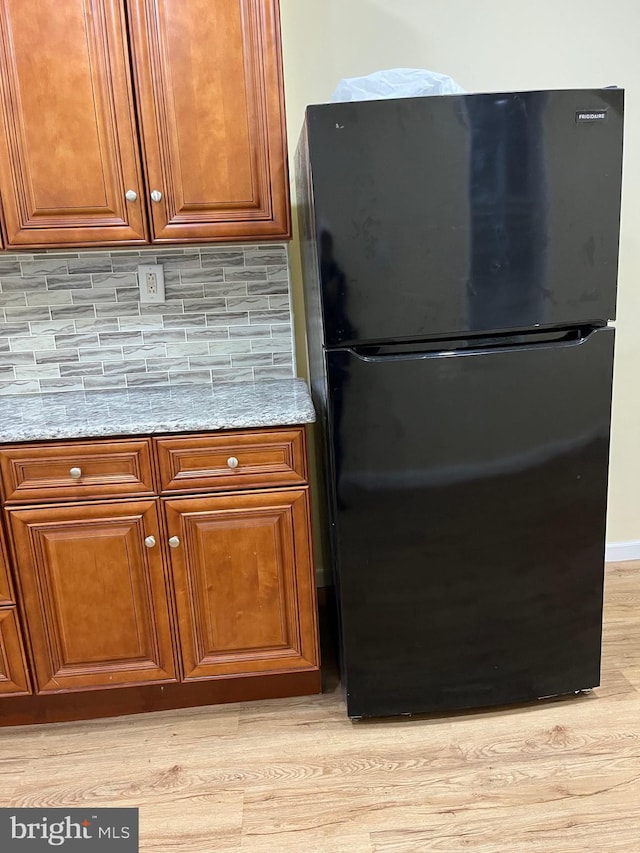 kitchen featuring black fridge, light stone counters, tasteful backsplash, and light hardwood / wood-style flooring