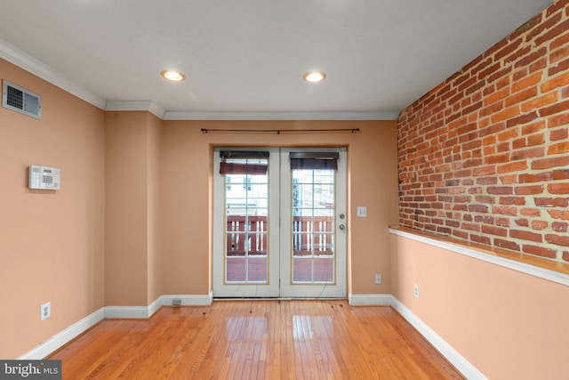 doorway to outside with light wood-type flooring, crown molding, brick wall, and french doors