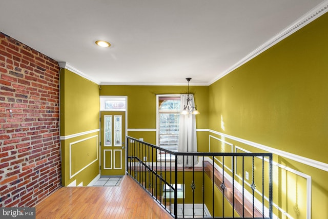 hall featuring hardwood / wood-style flooring, an inviting chandelier, brick wall, and ornamental molding