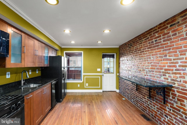 kitchen with black appliances, sink, dark stone countertops, light wood-type flooring, and brick wall