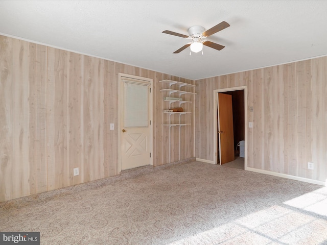 carpeted spare room featuring wooden walls and ceiling fan