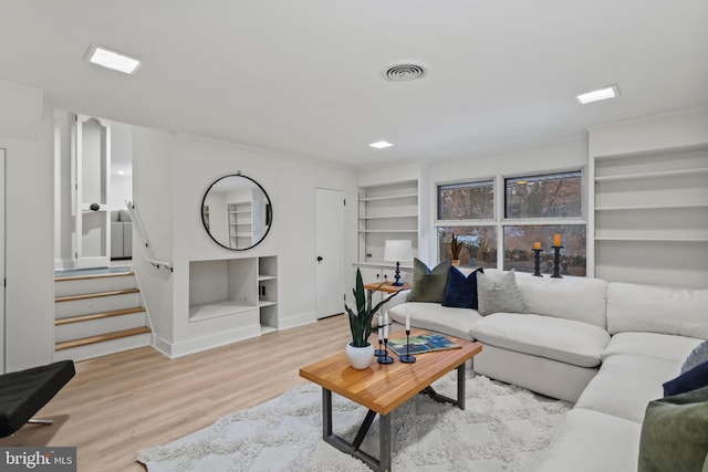 living room with built in shelves, crown molding, and light hardwood / wood-style flooring