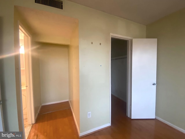 unfurnished bedroom with a walk in closet, a closet, and hardwood / wood-style flooring