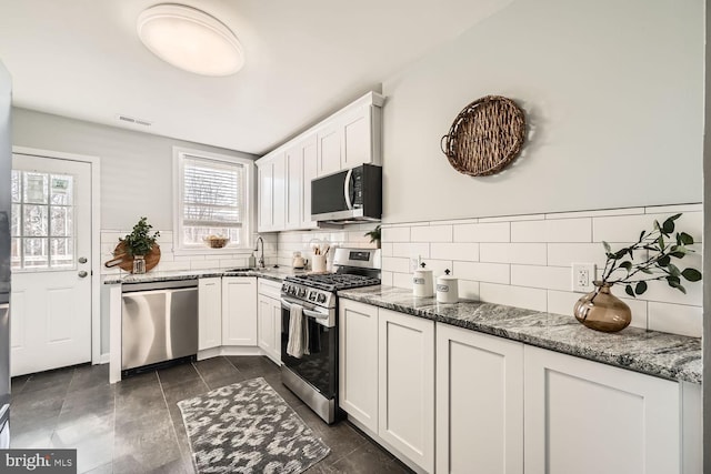 kitchen with dark stone countertops, appliances with stainless steel finishes, white cabinets, and a sink