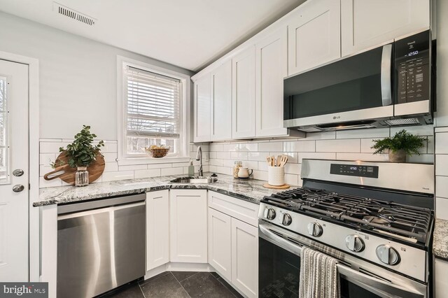 kitchen with visible vents, appliances with stainless steel finishes, light stone counters, white cabinetry, and a sink