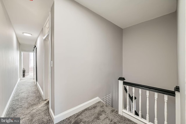 hallway featuring carpet, baseboards, and an upstairs landing