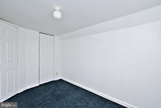 unfurnished bedroom with a closet, dark carpet, and vaulted ceiling