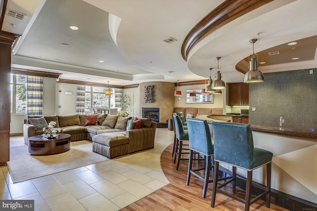 living room with a fireplace, light wood-type flooring, a raised ceiling, and ornamental molding