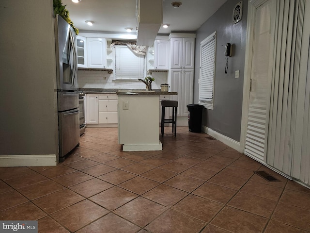 kitchen featuring a center island, a kitchen breakfast bar, tasteful backsplash, white cabinets, and dark tile patterned flooring