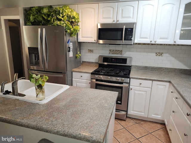 kitchen with sink, light tile patterned floors, appliances with stainless steel finishes, tasteful backsplash, and white cabinetry