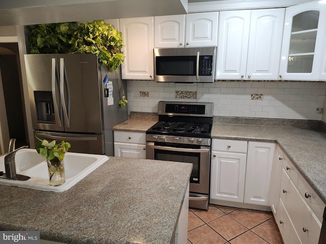 kitchen featuring sink, decorative backsplash, appliances with stainless steel finishes, light tile patterned flooring, and white cabinetry