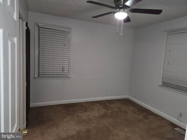 empty room featuring ceiling fan, dark carpet, and a textured ceiling