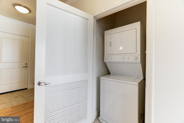 washroom featuring light tile patterned flooring, crown molding, and stacked washer and clothes dryer