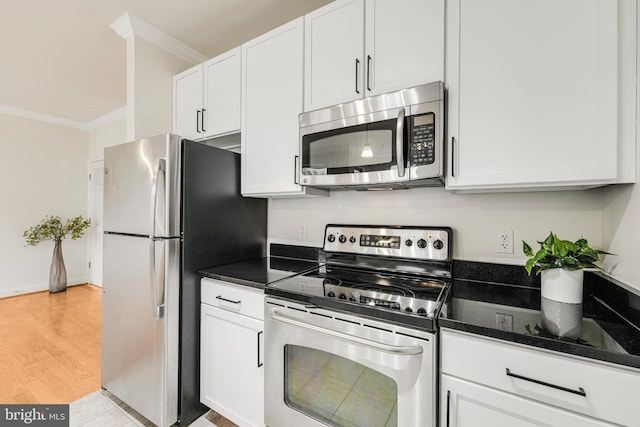 kitchen with white cabinetry, stainless steel appliances, ornamental molding, dark stone countertops, and light wood-type flooring