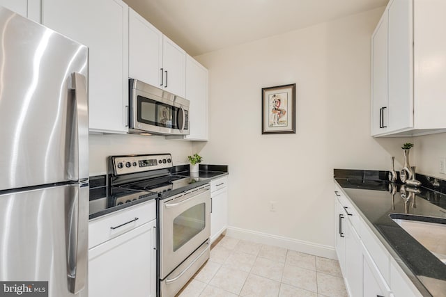 kitchen with white cabinetry, sink, dark stone counters, light tile patterned floors, and appliances with stainless steel finishes