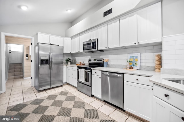 kitchen with light tile patterned floors, stainless steel appliances, backsplash, white cabinetry, and vaulted ceiling