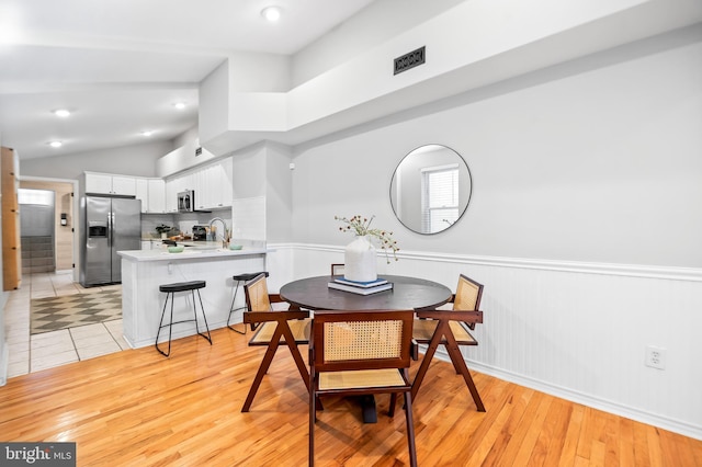 dining area featuring light wood-style floors, lofted ceiling, a wainscoted wall, and recessed lighting