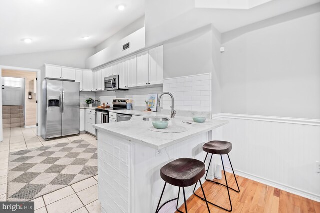 kitchen featuring lofted ceiling, appliances with stainless steel finishes, a peninsula, light stone countertops, and a sink