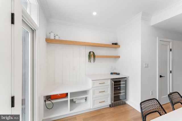 bar with white cabinetry, light hardwood / wood-style flooring, beverage cooler, and ornamental molding