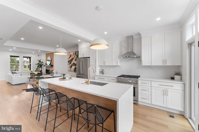 kitchen featuring wall chimney exhaust hood, pendant lighting, high quality appliances, white cabinets, and an island with sink