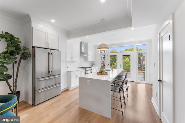 kitchen featuring a center island, high quality appliances, white cabinets, wall chimney exhaust hood, and decorative light fixtures