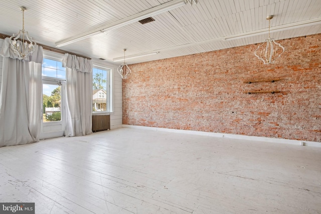 spare room with a chandelier, radiator heating unit, hardwood / wood-style floors, and brick wall