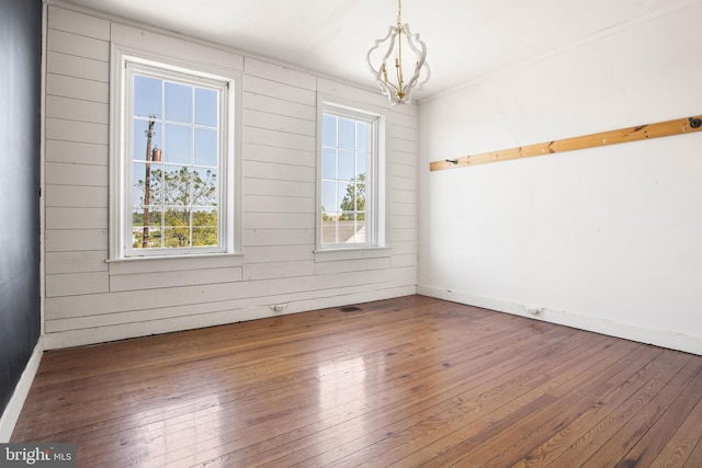 empty room featuring wooden walls, dark hardwood / wood-style flooring, and an inviting chandelier