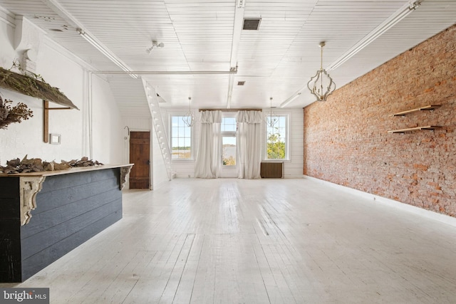 unfurnished living room with radiator heating unit, brick wall, and light hardwood / wood-style floors