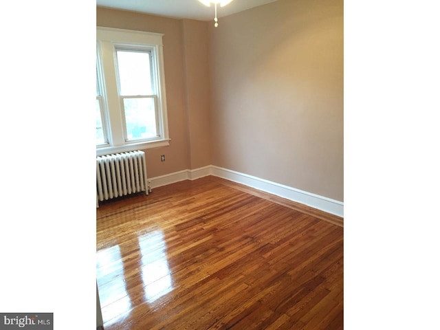 unfurnished room featuring radiator heating unit and hardwood / wood-style floors