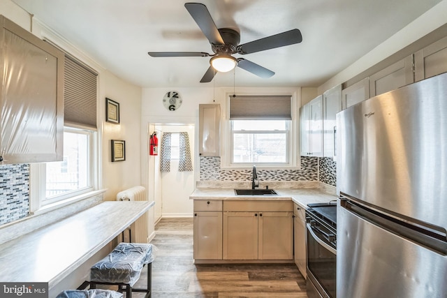 kitchen with black stove, sink, stainless steel fridge, light brown cabinetry, and plenty of natural light