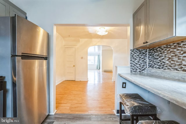 kitchen with decorative backsplash, gray cabinets, light wood-type flooring, and stainless steel refrigerator