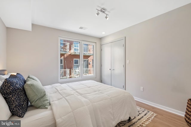 bedroom with track lighting, a closet, and light hardwood / wood-style flooring