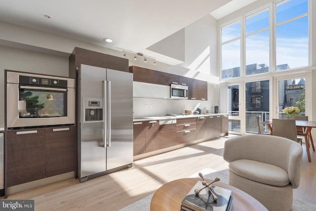 kitchen featuring light wood-type flooring, a towering ceiling, dark brown cabinetry, and appliances with stainless steel finishes