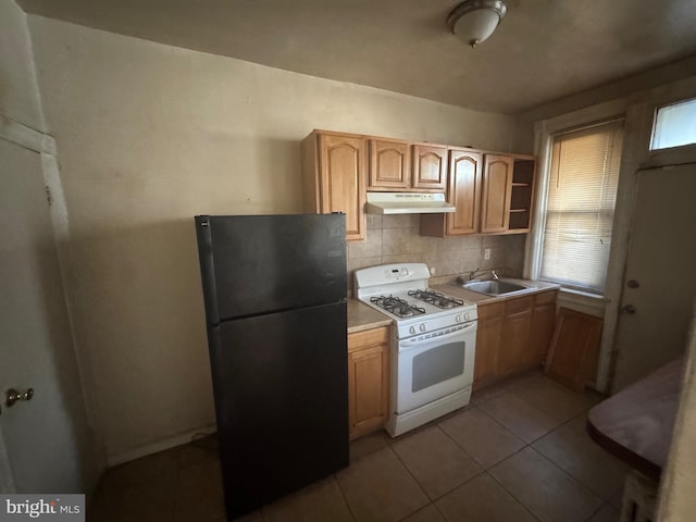 kitchen with black refrigerator, sink, decorative backsplash, gas range gas stove, and light tile patterned flooring