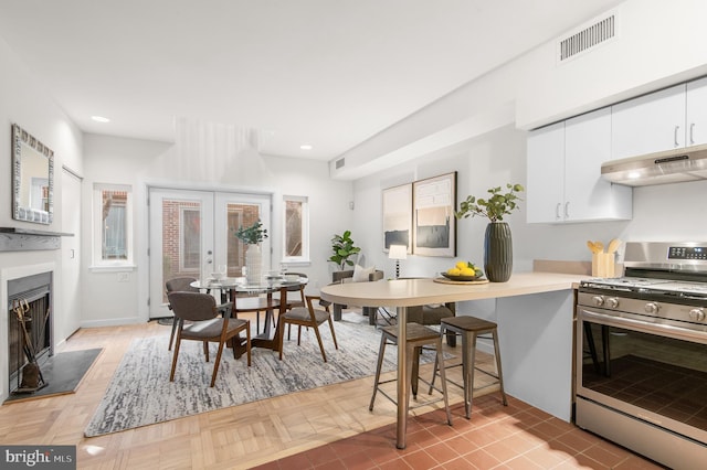 kitchen with stainless steel range, french doors, ventilation hood, and white cabinetry