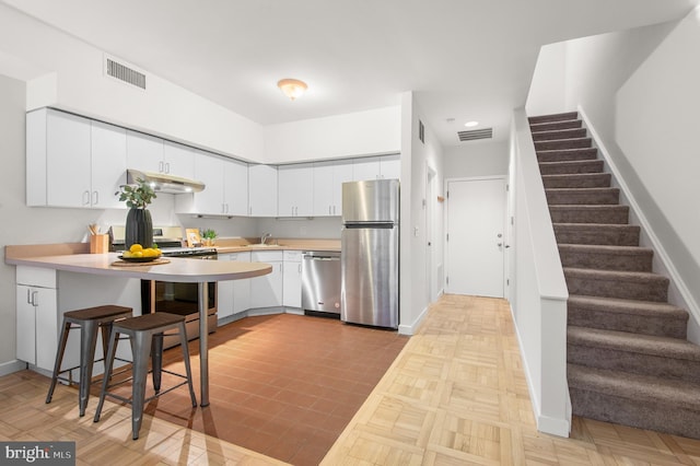 kitchen featuring a breakfast bar, stainless steel appliances, light parquet floors, sink, and white cabinets