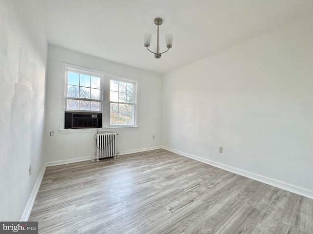 unfurnished room featuring cooling unit, light wood-type flooring, radiator heating unit, and a chandelier