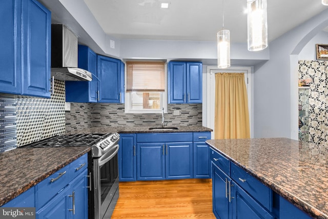 kitchen featuring wall chimney range hood, gas stove, blue cabinetry, and sink