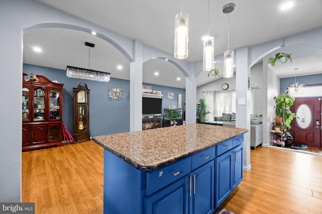 kitchen with pendant lighting, a center island, light stone countertops, blue cabinets, and light wood-type flooring