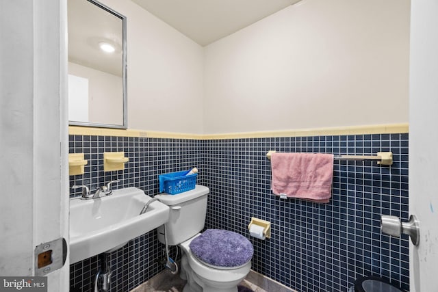 bathroom with toilet, sink, and tile walls