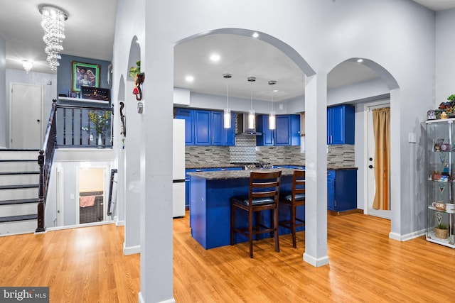 kitchen featuring wall chimney range hood, a breakfast bar area, white fridge, blue cabinets, and light wood-type flooring