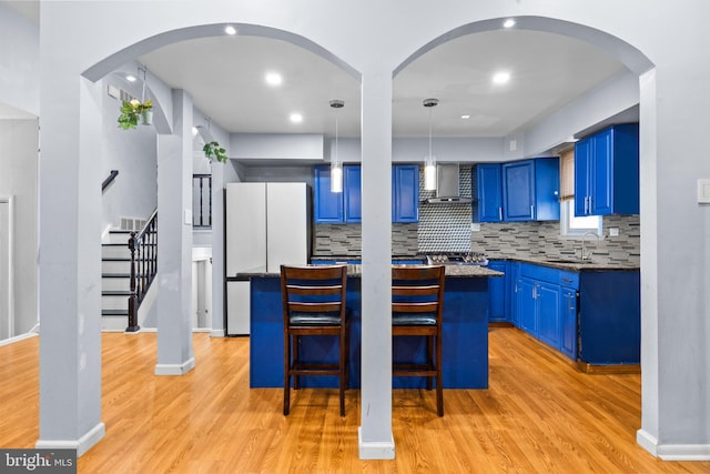 kitchen with pendant lighting, blue cabinets, white refrigerator, a center island, and wall chimney exhaust hood