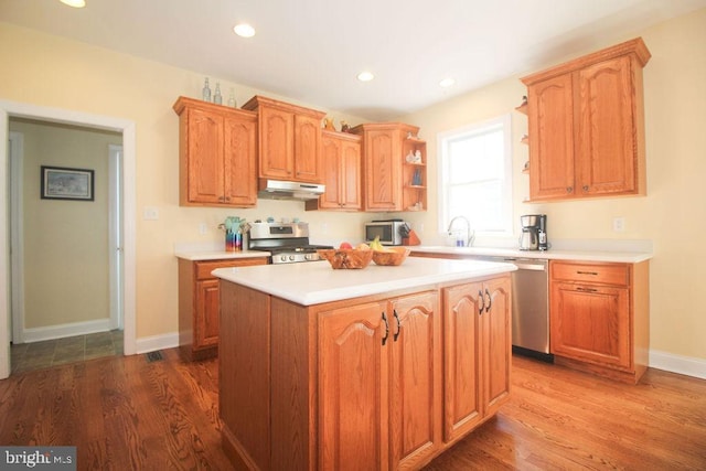 kitchen with sink, a kitchen island, wood-type flooring, and appliances with stainless steel finishes