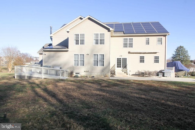 rear view of property with a patio area, a yard, a deck, and solar panels