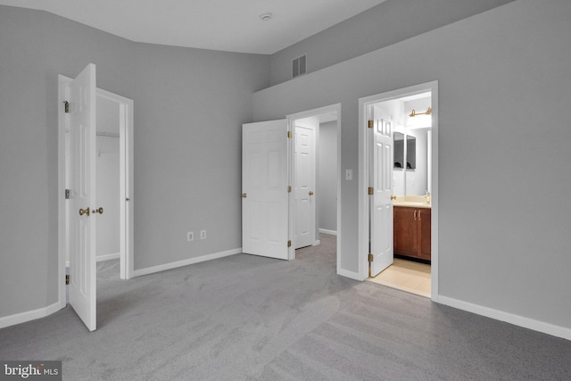 unfurnished bedroom featuring light carpet, vaulted ceiling, and ensuite bath