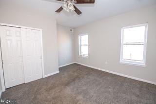 unfurnished bedroom with ceiling fan, a closet, and dark colored carpet